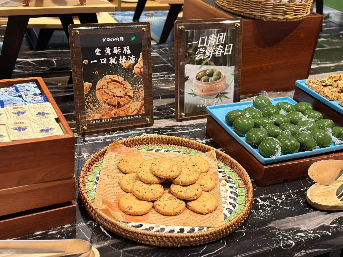 A display of food items including cookies, green balls, and a sign with Chinese text.