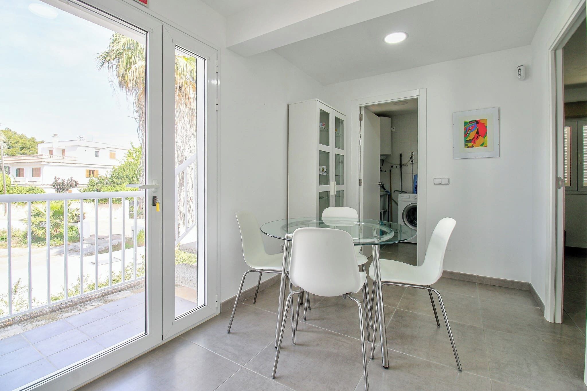 A modern dining area with a glass table and white chairs, a glass cabinet, and a view of the outside.