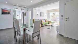 Un salon moderne avec une table à manger en verre, des canapés blancs et une grande fenêtre.