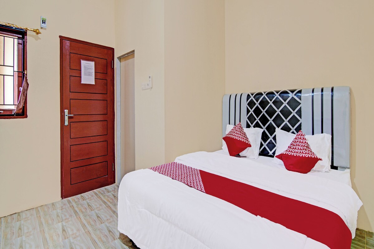A hotel room with a bed, a wooden door, and a window with bars.