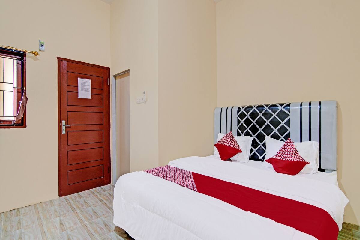 A hotel room with a large bed, a wooden door, and a window with bars.