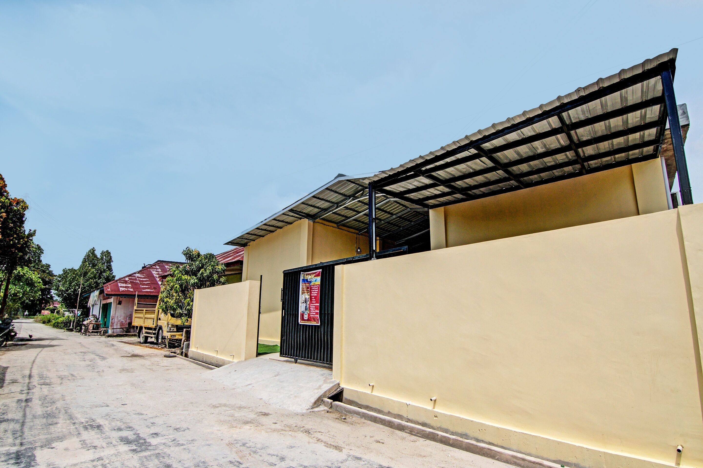 A residential area with a gated entrance, a yellow building, and a red-roofed structure in the background.