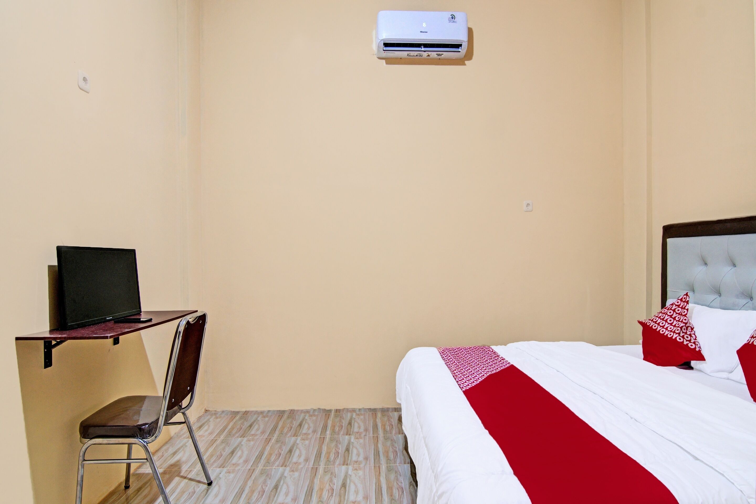 A bedroom with a bed, a desk with a chair, and an air conditioner.