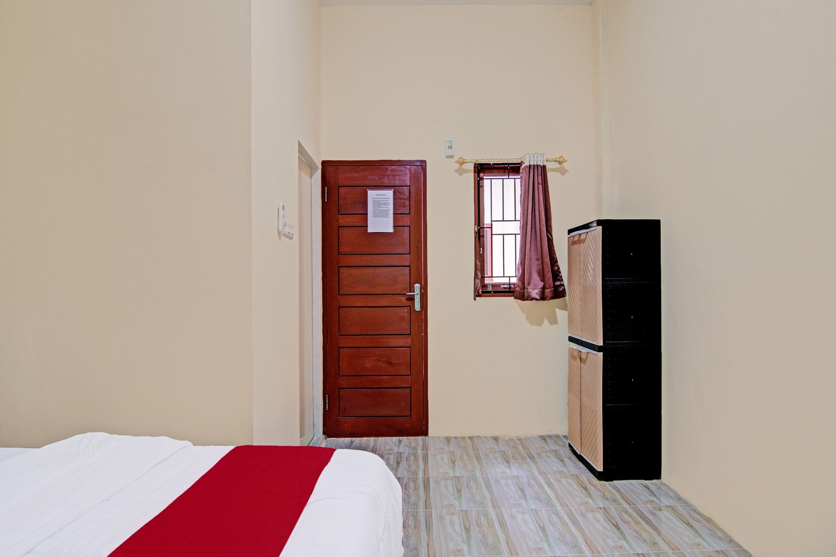 Un dormitorio con cama, una puerta de madera, una ventana con cortinas y un armario.
