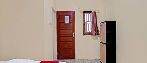 Un dormitorio con cama, una puerta de madera, una ventana con cortinas y un armario.
