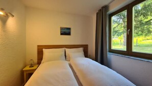 Camera d'albergo con un letto, un comodino, un quadro e una finestra vista verde.