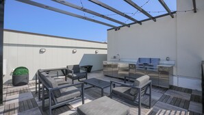A rooftop patio with outdoor furniture, a grill, and a small potted plant. - Penthouse w Rooftop, Private Chef, Secure Parking (Atlanta)
