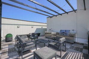 A rooftop patio with outdoor furniture, a grill, and a small potted plant.
