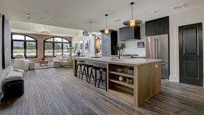 A modern kitchen with a central island, bar stools, and a large window overlooking a patio area. - Penthouse w Rooftop, Private Chef, Secure Parking (Atlanta)