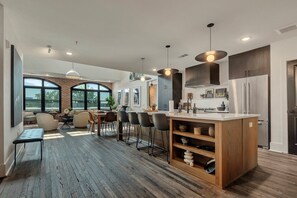 A modern kitchen with a central island, bar stools, and a dining area with a large window.