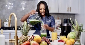 A kitchen with a modern design, featuring a stainless steel sink, a coffee maker, and a variety of fruits and vegetables on the counter.