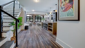 A spacious living area with a wooden floor, a staircase, and a kitchen area with bar stools. - Penthouse w Rooftop, Private Chef, Secure Parking (Atlanta)