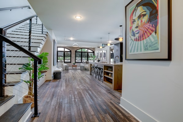 A spacious living area with a wooden floor, a staircase, and a kitchen area with bar stools.