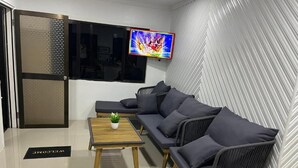 Un espace de détente moderne comprenant un ensemble de canapés, une petite table en bois avec une plante et un téléviseur fixé au mur.