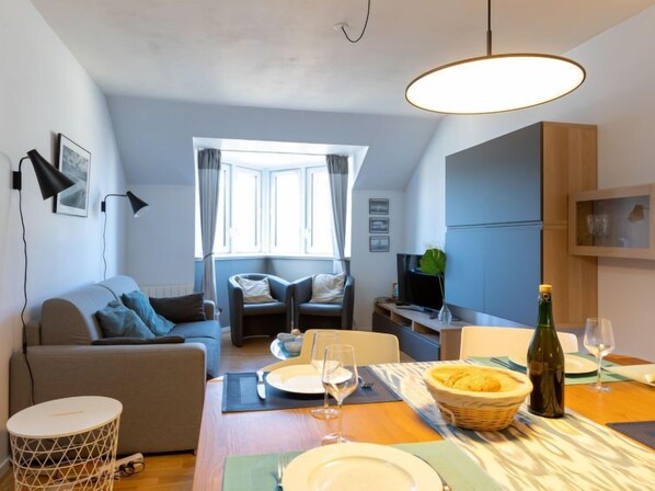 A modern living room with a sofa, dining table set for two, and a television.