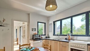 Una cocina moderna con una mesa de comedor de madera, armarios blancos, horno empotrado y amplias ventanas con vistas al exterior.
