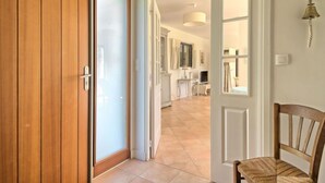 Un pasillo con una puerta de madera, una puerta blanca y una silla.