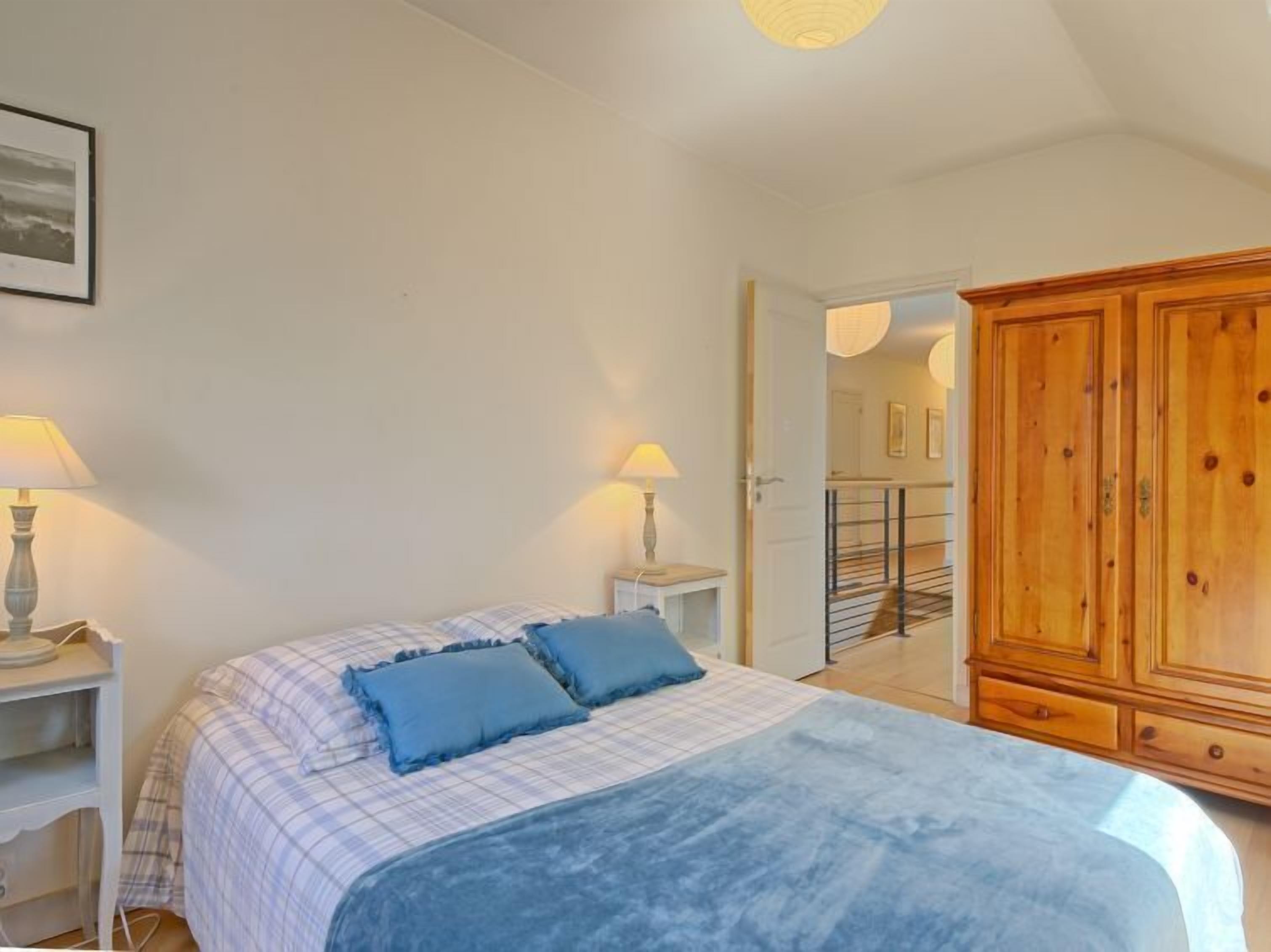 A bedroom with a bed, two bedside lamps, a wardrobe, and a door leading to a staircase.
