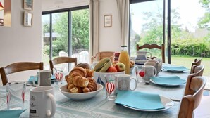 Una mesa de desayuno dispuesta con cruasanes, frutas y tazas de café, con vistas a un jardín.