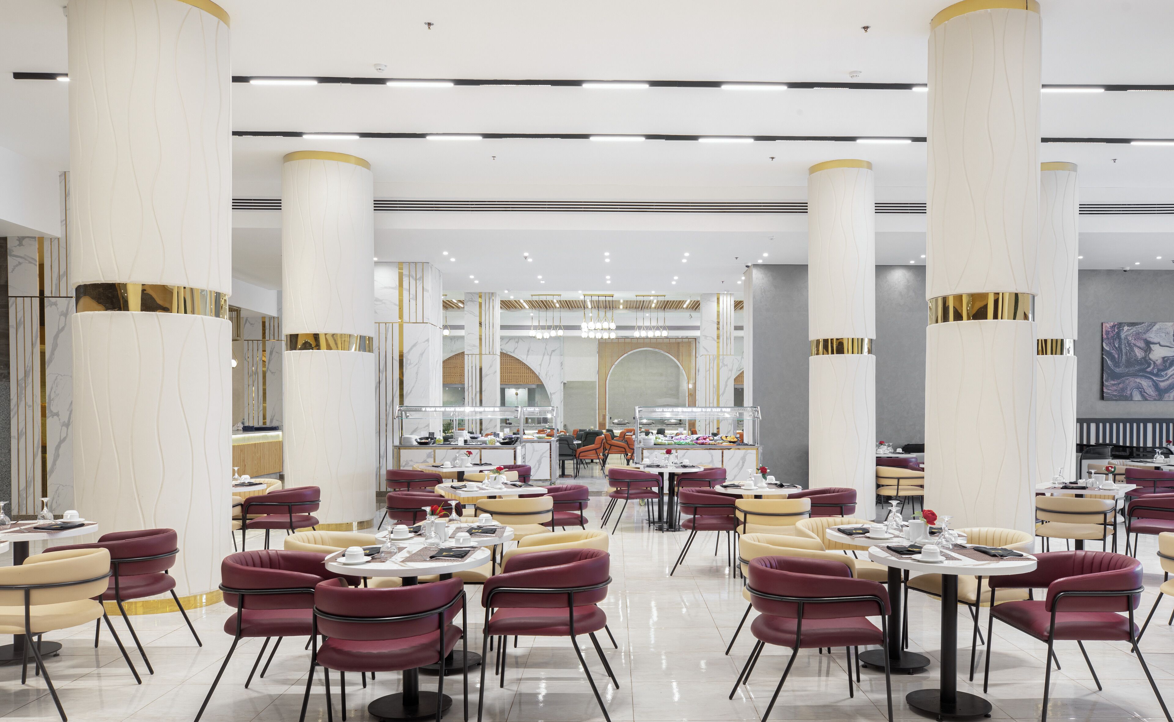 Un espace de restauration moderne avec des tables et des chaises rondes, de grandes colonnes décoratives et un îlot central pour le service.