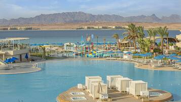 A resort pool area with a wooden deck, lounge chairs, umbrellas, and a view of the mountains.