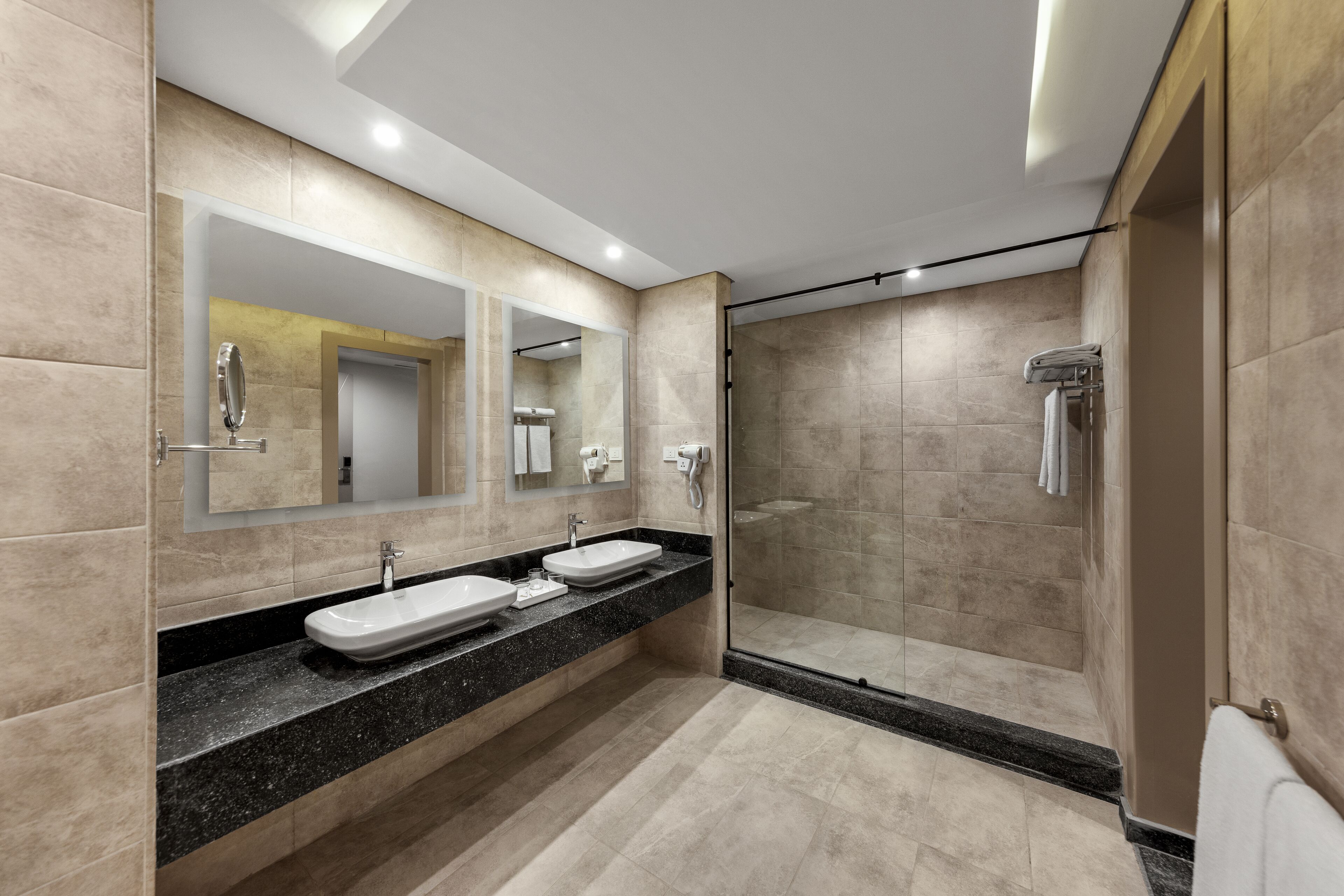 A modern bathroom with two sinks, a large mirror, and a walk-in shower.