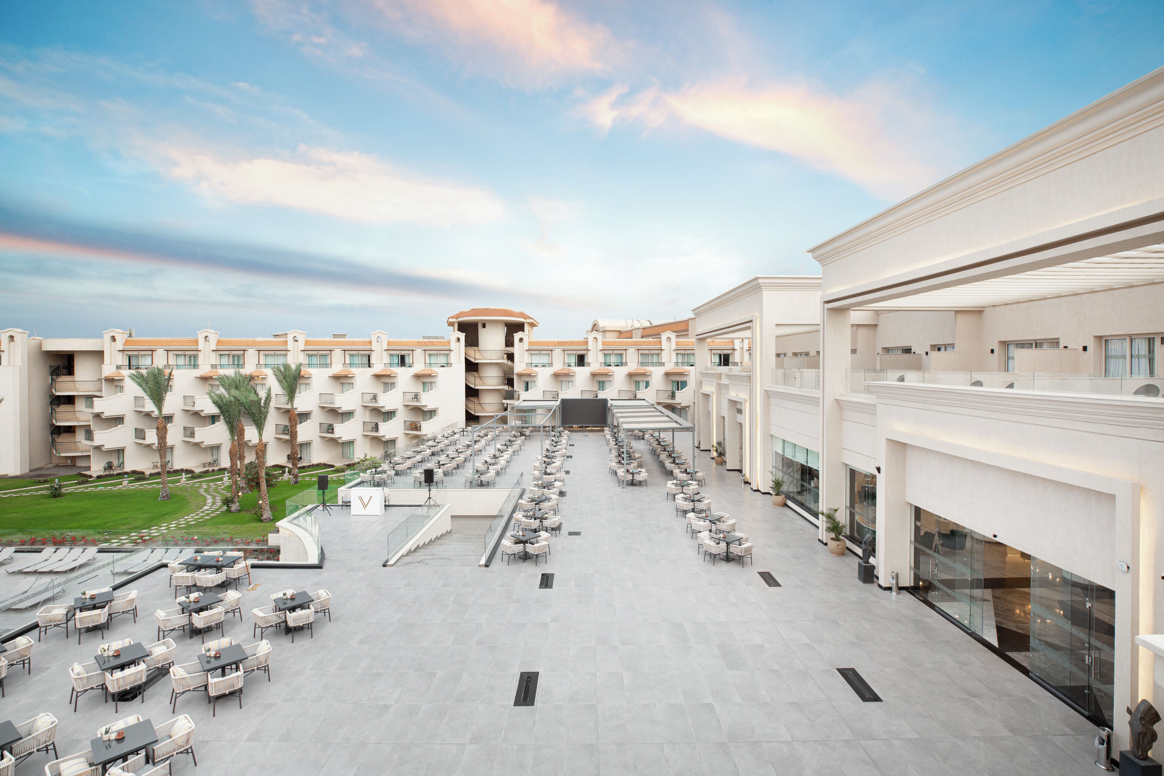 Un patio de hotel con mobiliario exterior, una escalera central y varios balcones.