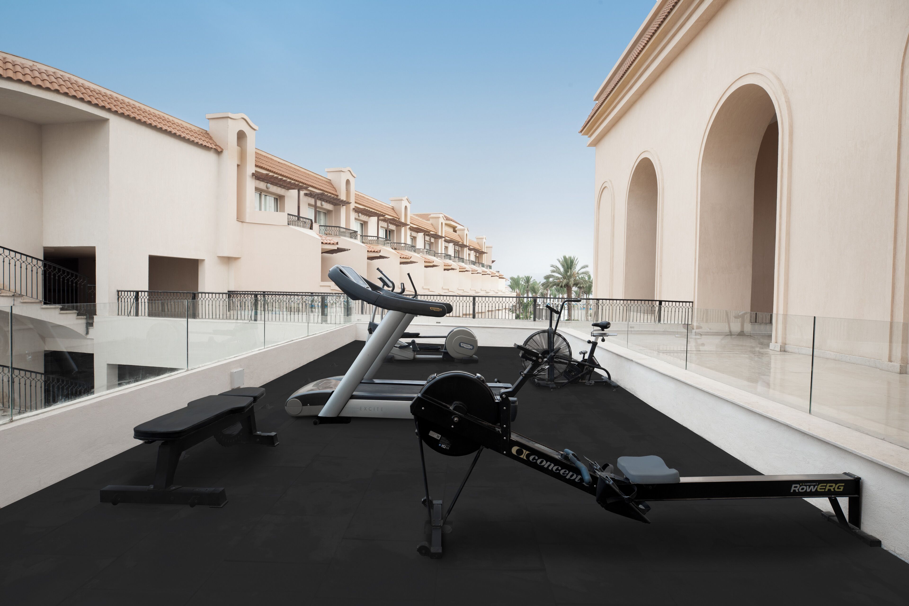 Un gimnasio en la azotea con equipo de ejercicio, una banca y vistas a los edificios del hotel.