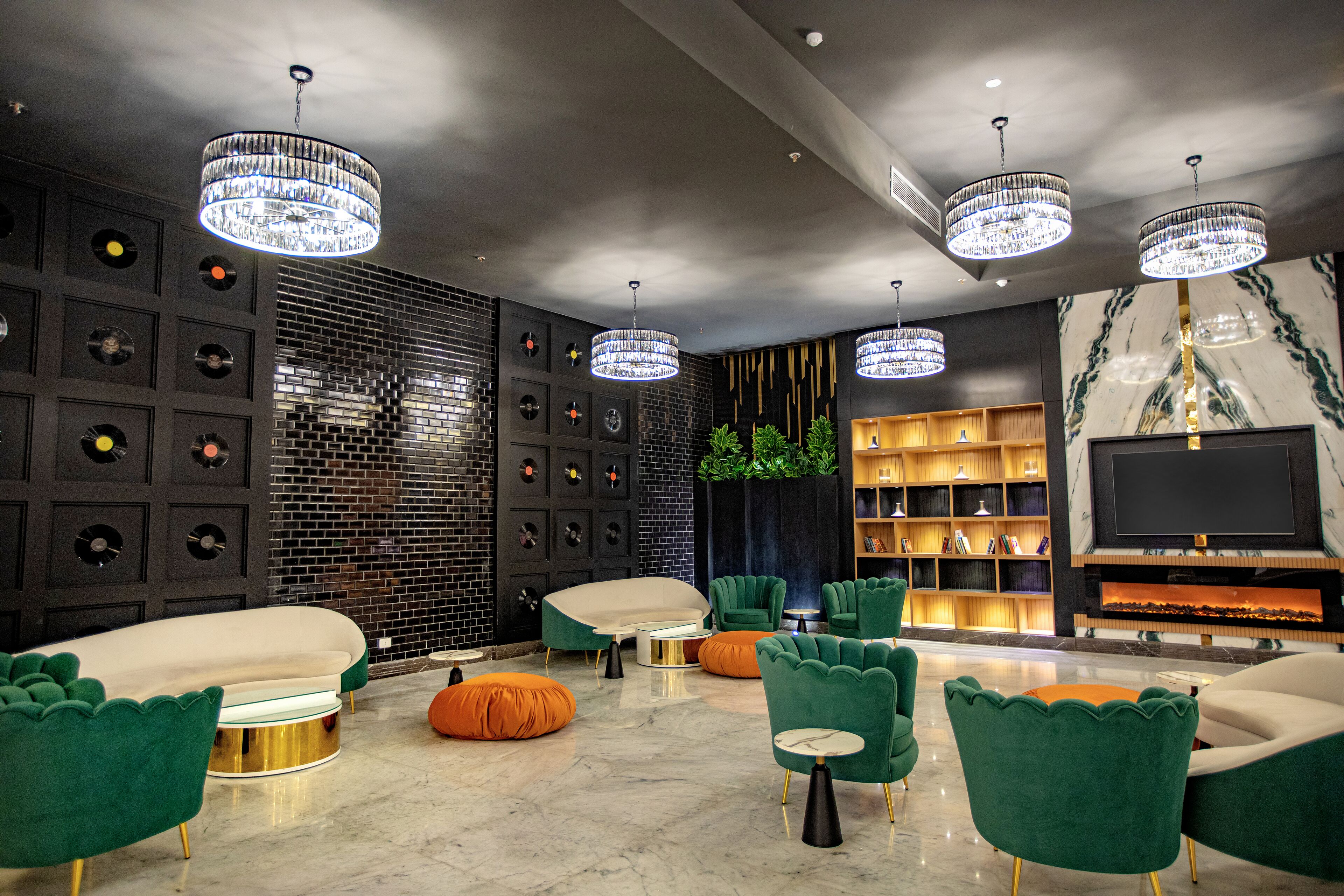 A modern lounge area with green upholstered sofas, a marble floor, and a wall adorned with vinyl records and a TV.