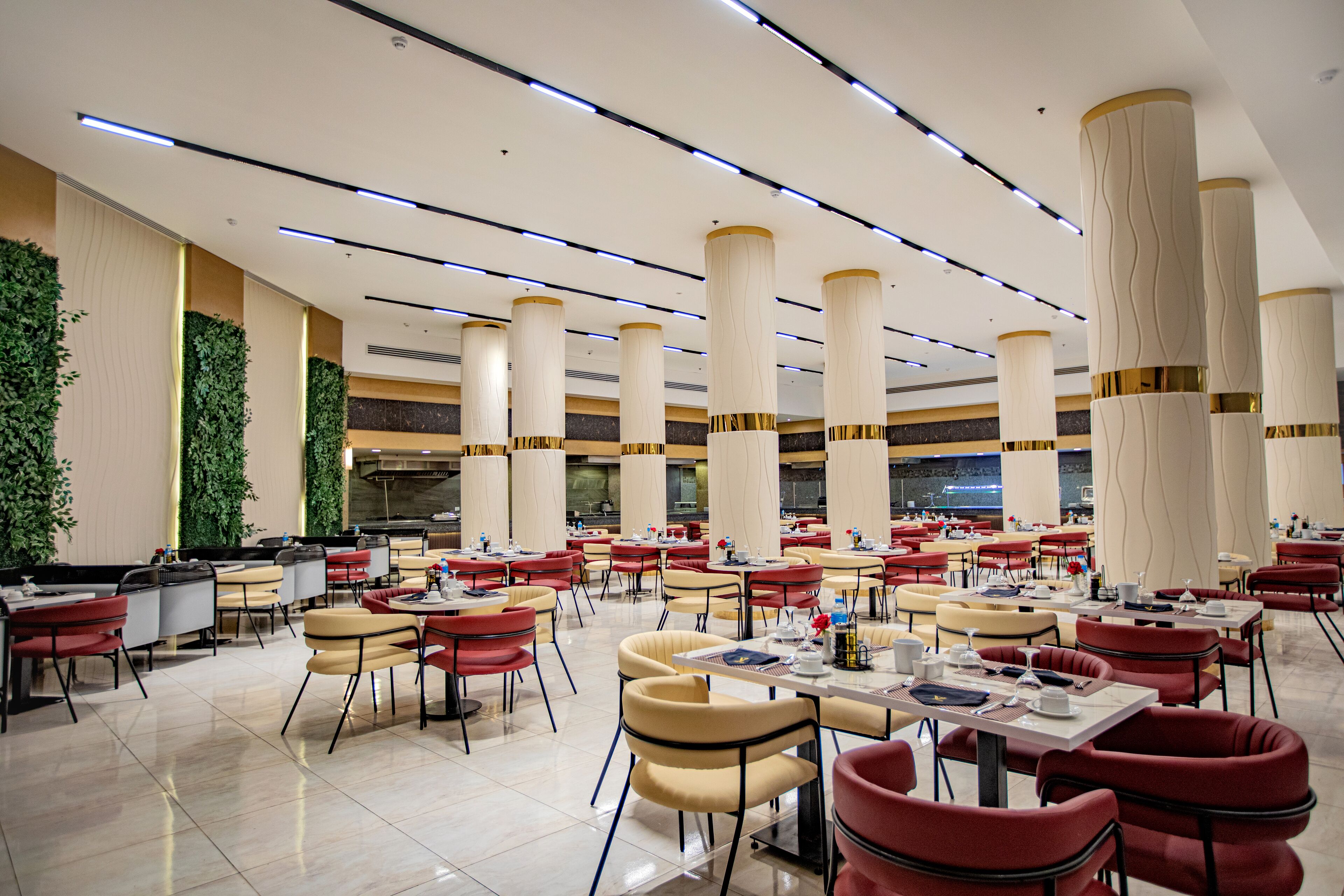 Un comedor amplio con varias mesas y sillas, techo alto con iluminación moderna y columnas decorativas.