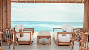 Un espacio de descanso frente a la playa con dos sillones acolchados y una mesa de madera, con vistas al océano.