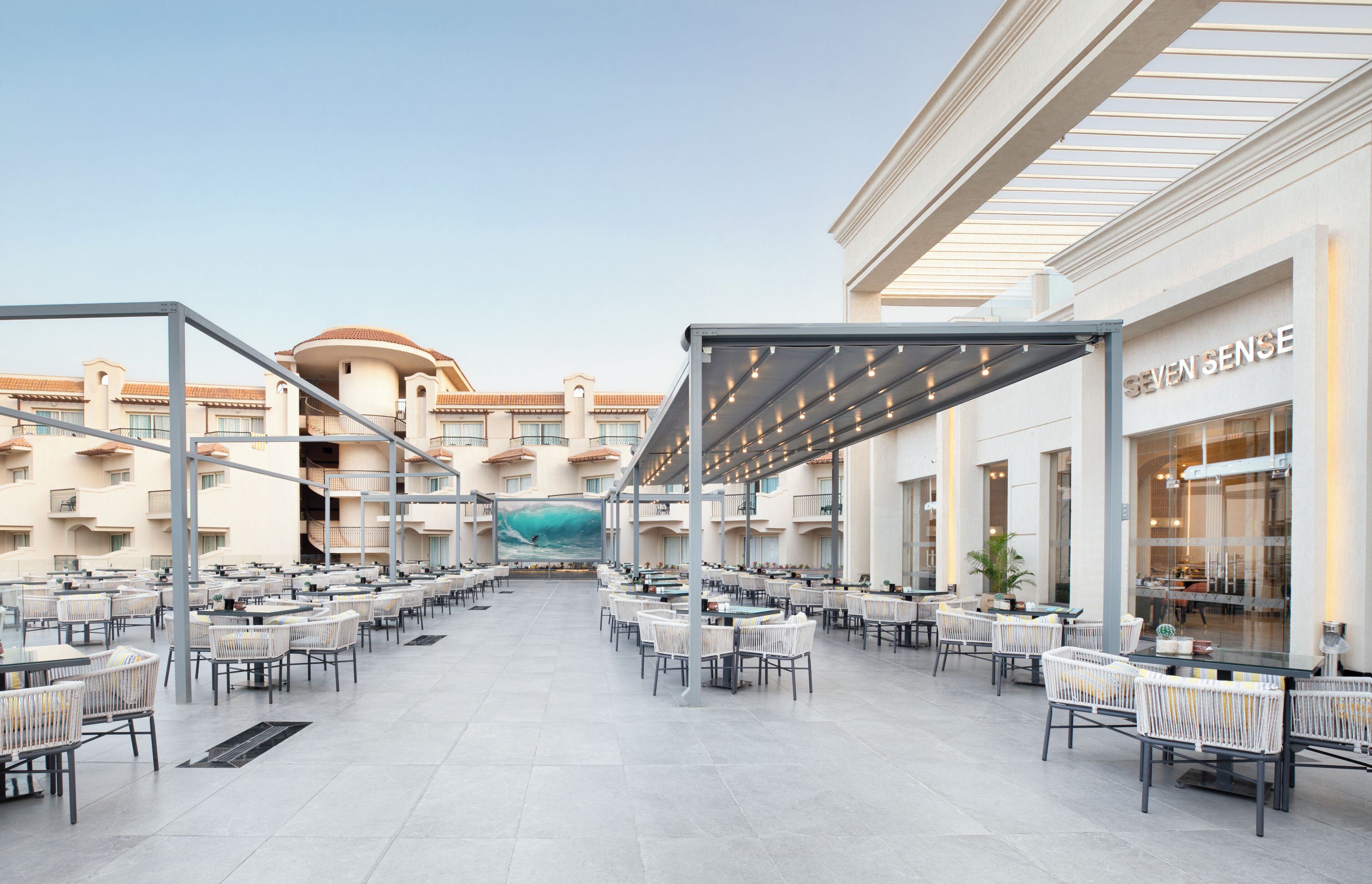 A spacious outdoor patio with multiple tables and chairs, a large mural, and a restaurant named SEVEN SENSE.