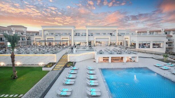 Un hotel con piscina en la azotea, mobiliario exterior y un edificio grande con varios balcones.