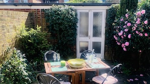 A patio with a wooden table and chairs, a yellow bowl, two glasses, and a green candle. - Beautiful Cottage in the heart of Lytham. (Lytham St.Annes)