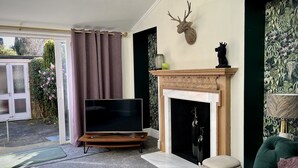 A living room with a fireplace, a mounted deer head, a television on a wooden stand, and a green sofa. - Beautiful Cottage in the heart of Lytham. (Lytham St.Annes)