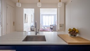 A modern kitchen with a central island, a built-in sink, pendant lighting, and a view into the dining area. - Dreaming in the Daytime, by Veeve (Paris)