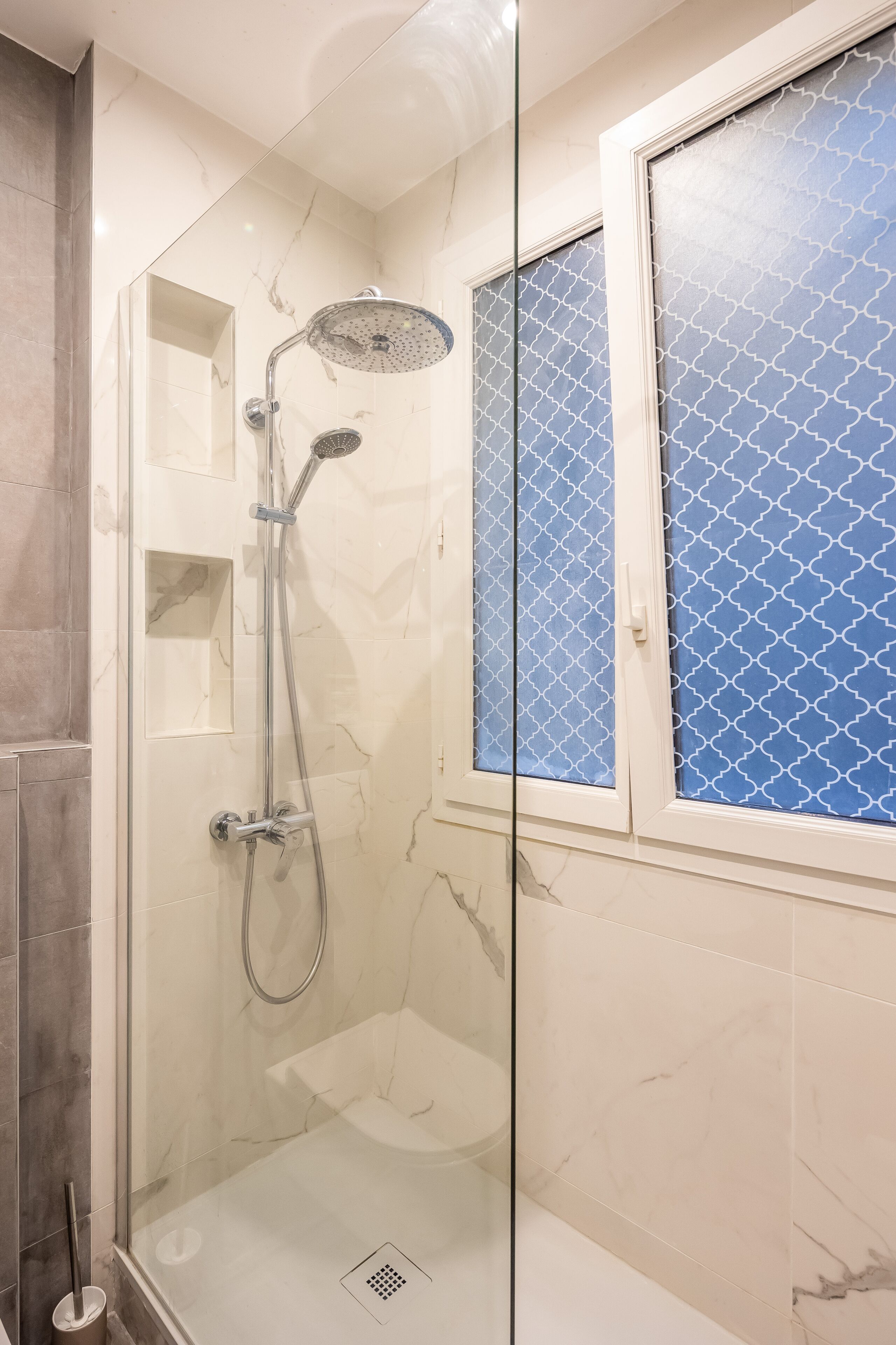 A glass-enclosed shower with a handheld showerhead and a wall-mounted faucet.