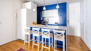 A modern kitchen with a blue accent wall, white bar stools, and a central island. - Dreaming in the Daytime, by Veeve (Paris)