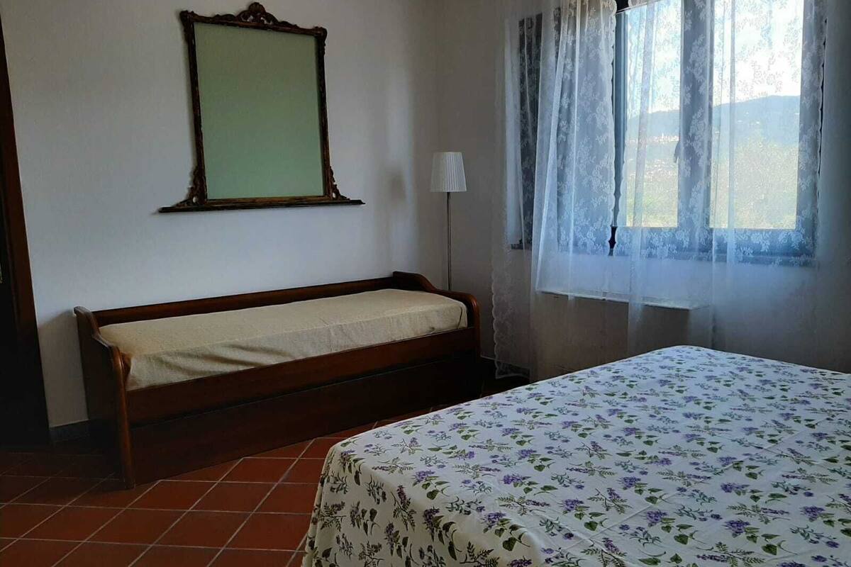 A room with a bed, a bench, a mirror, a lamp, and a window with curtains.
