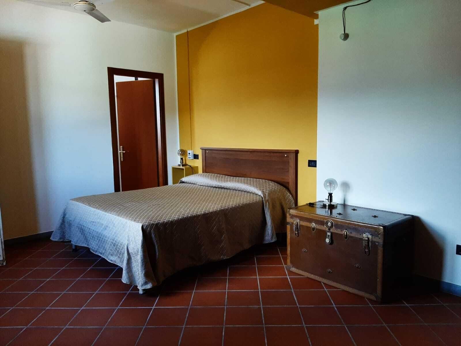 A bedroom with a bed, a wooden headboard, a suitcase, and a wall-mounted light fixture.