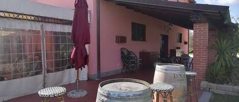 A pink building with a covered patio area featuring two wooden barrels and stools.