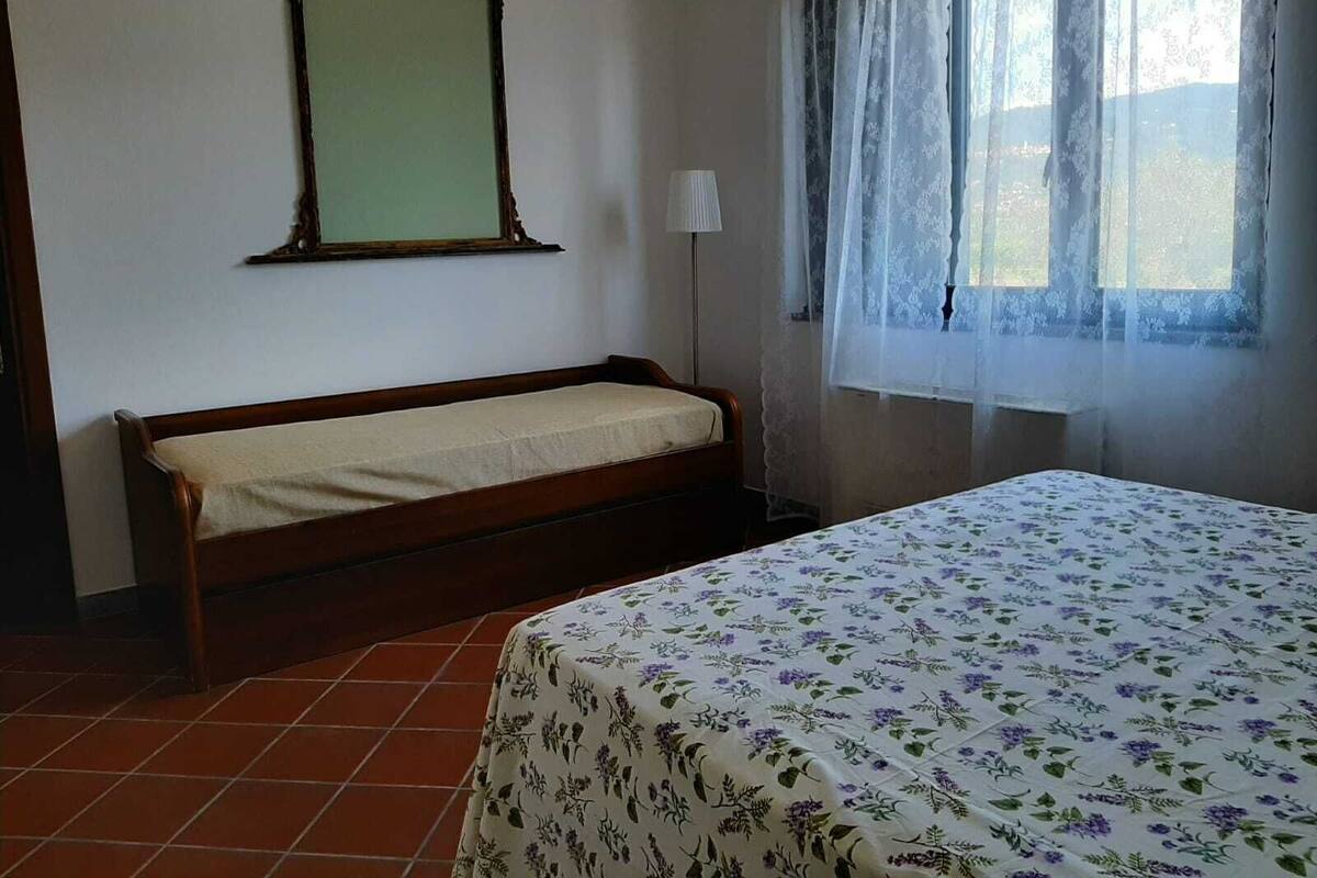 A room with a bed, a bench, a mirror, and a window with curtains.