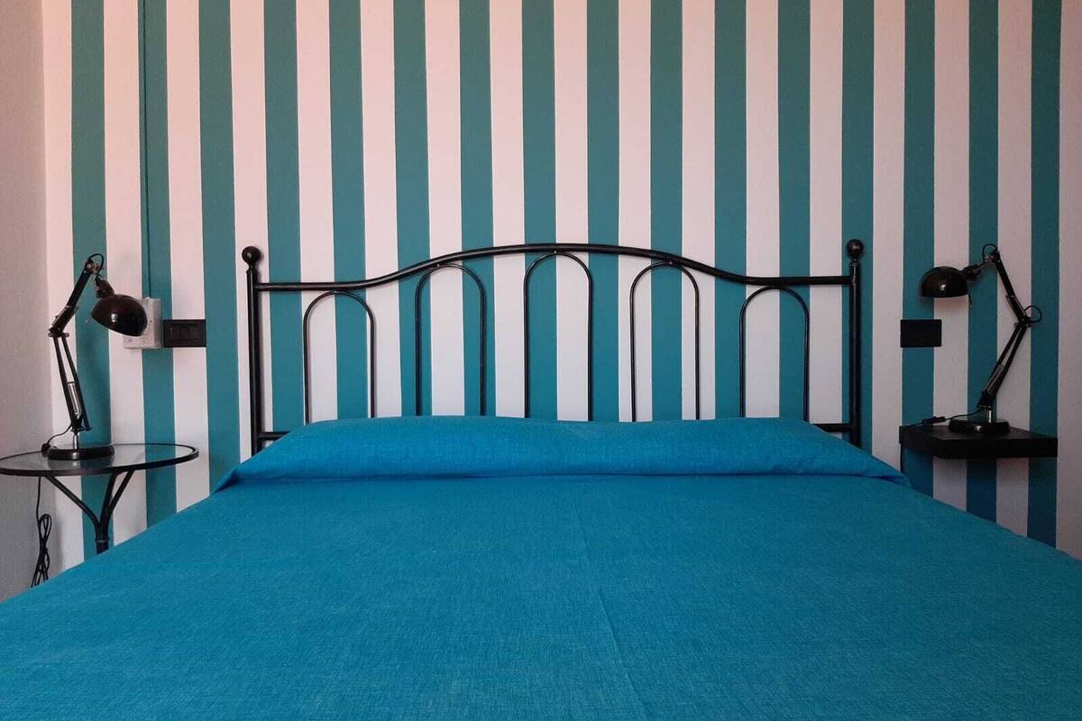 A bed with a blue mattress in a room with striped wallpaper.