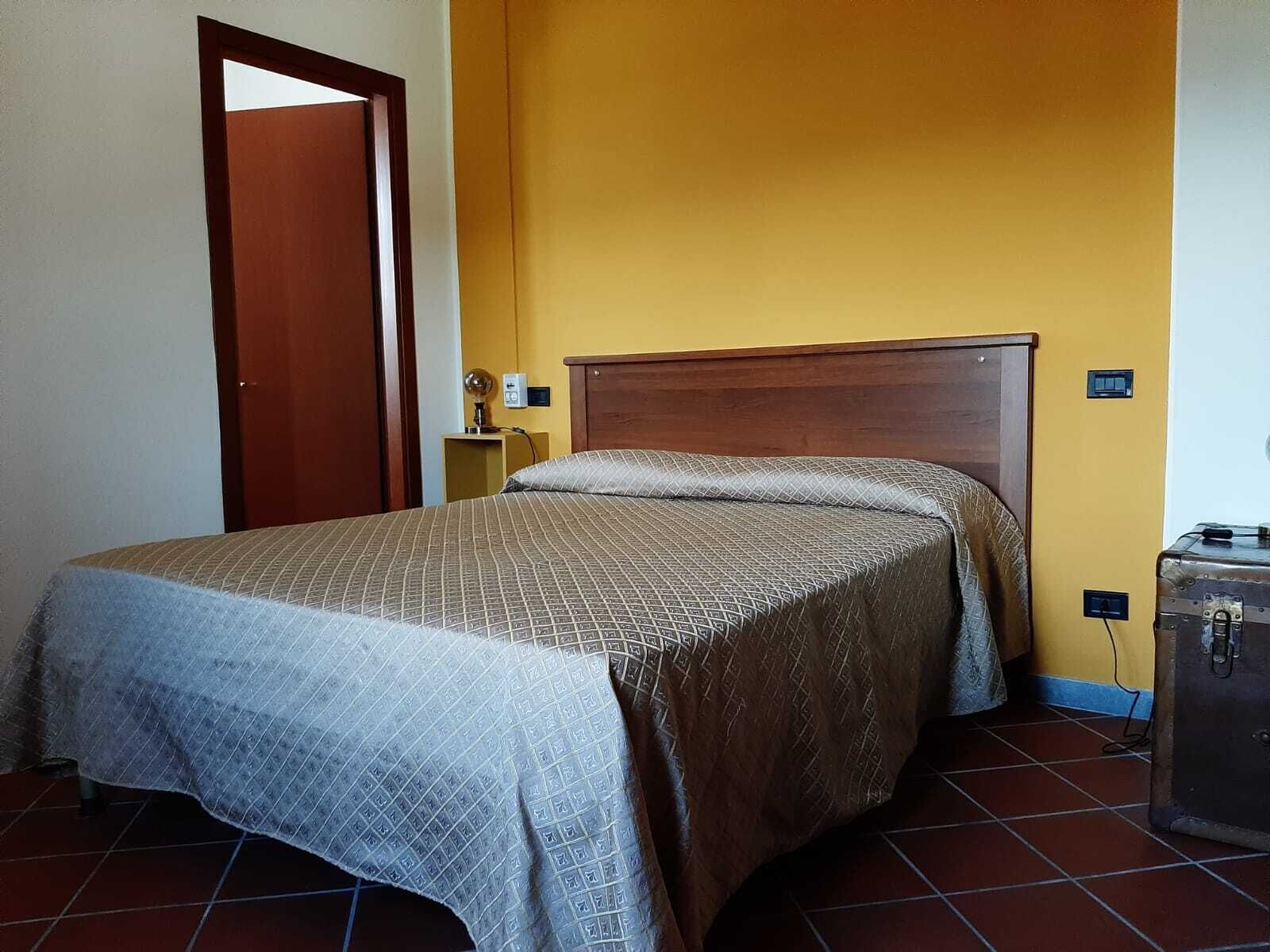 A bedroom with a bed, a nightstand, a lamp, and a suitcase.