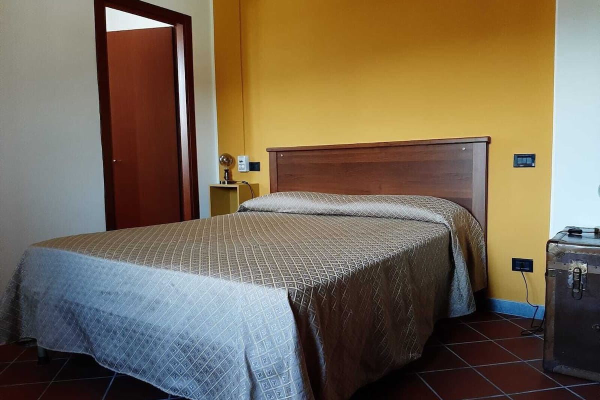 A single bed with a wooden headboard in a room with yellow walls and a tiled floor.