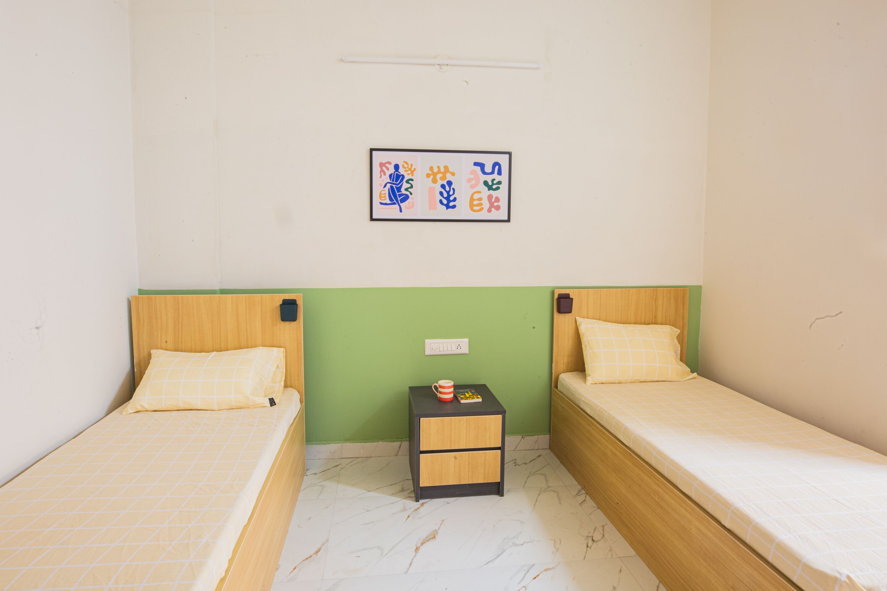 Una habitación pequeña y limpia con dos camas individuales, una mesita de noche y una obra de arte colgada en la pared.
