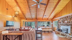 Eine geräumige Holzhütte mit Holzvertäfelung, einem Kamin aus Stein, einem Deckenventilator und einem Fernseher.