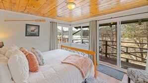 Ein Schlafzimmer mit Holzboden, einem großen Bett, einem Fenster mit Blick ins Freie und einem Bild an der Wand.