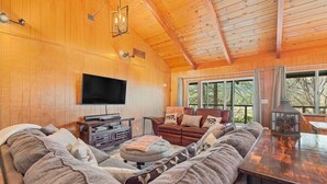 Ein gemütliches Wohnzimmer mit Holzvertäfelung, einem Flachbildfernseher, einem Ledersofa und einem Essbereich mit Holztisch.