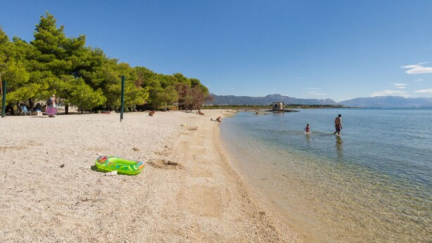 Une plage avec une eau claire et peu profonde, des arbres et quelques personnes.